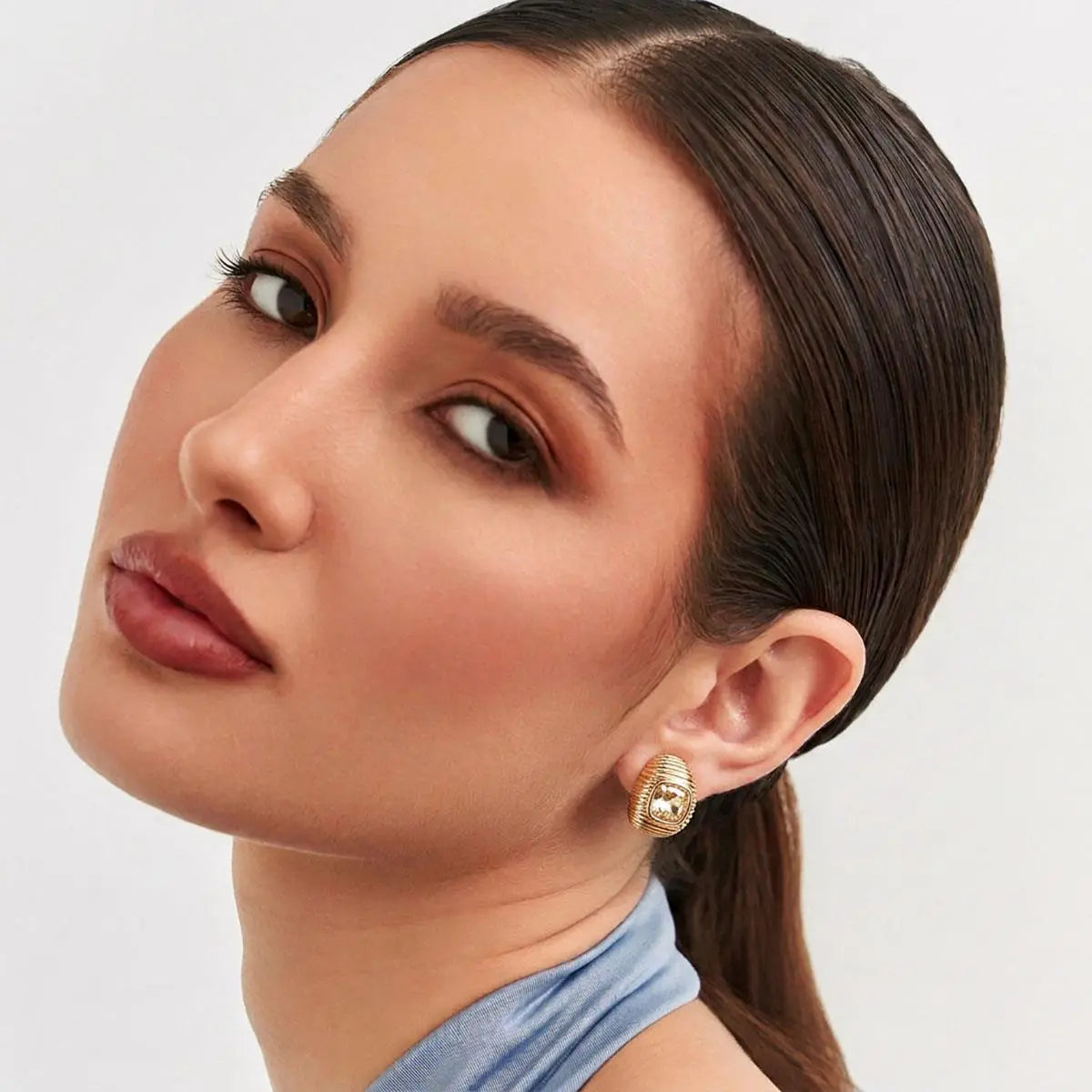 Close-up of a woman wearing gold hoop earrings with a neutral background