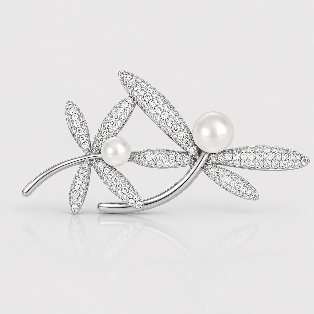 A silver-toned floral brooch featuring two flower motifs paved with clear crystals and accented with two white pearls, shown on a light gray reflective background.