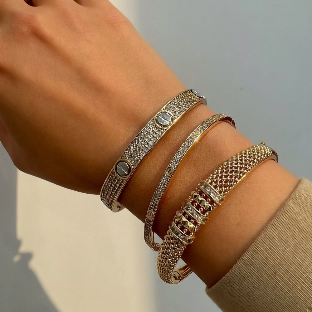 Hand wearing multiple gold and silver bracelets on a neutral background