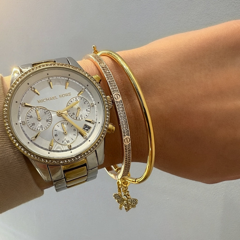 Gold watch and bracelet on a wrist against a neutral background