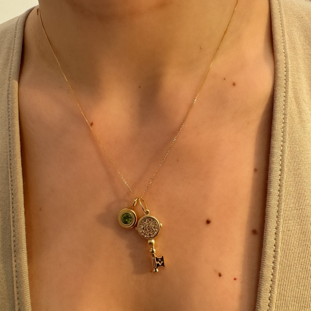 Gold necklace with a pendant on a person wearing a beige cardigan.