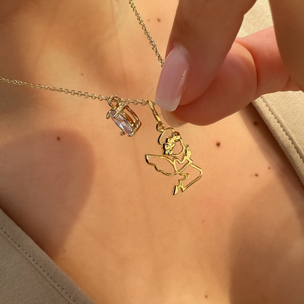 Gold necklace with a pendant held by a hand against a neutral background