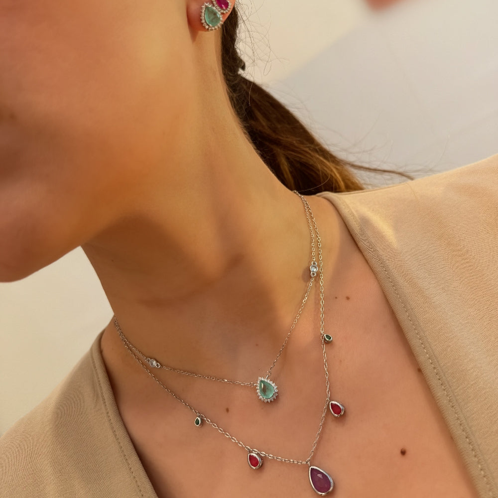 Close-up of a person wearing a necklace and earrings with gemstones.