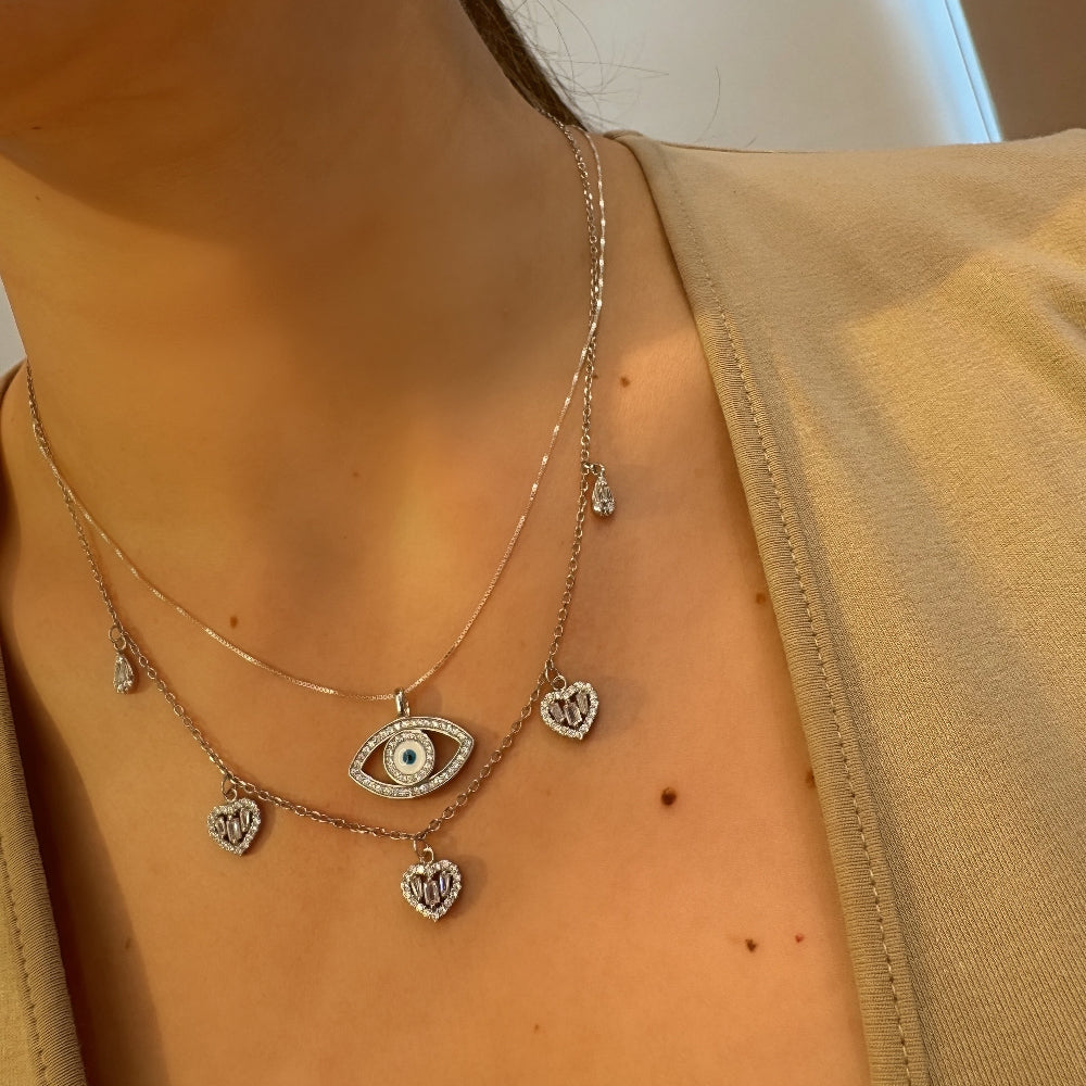 Necklace with eye and heart charms on a person wearing a beige top.