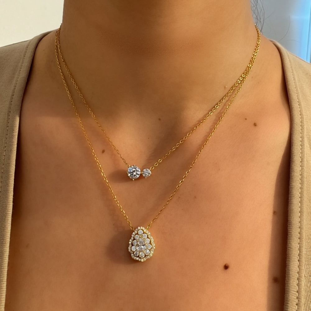 Gold necklace with a diamond pendant worn by a person, with a blurred background.