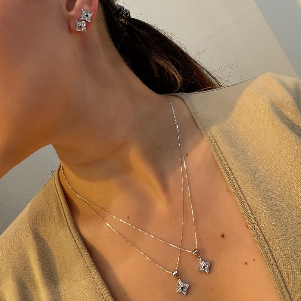 Close-up of a person wearing silver earrings and a necklace with star-shaped pendants.