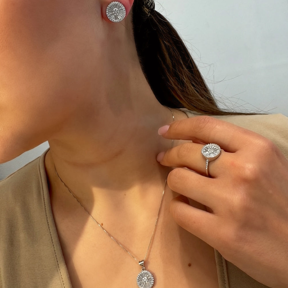 Close-up of a person wearing silver earrings and a ring, with a neutral background.
