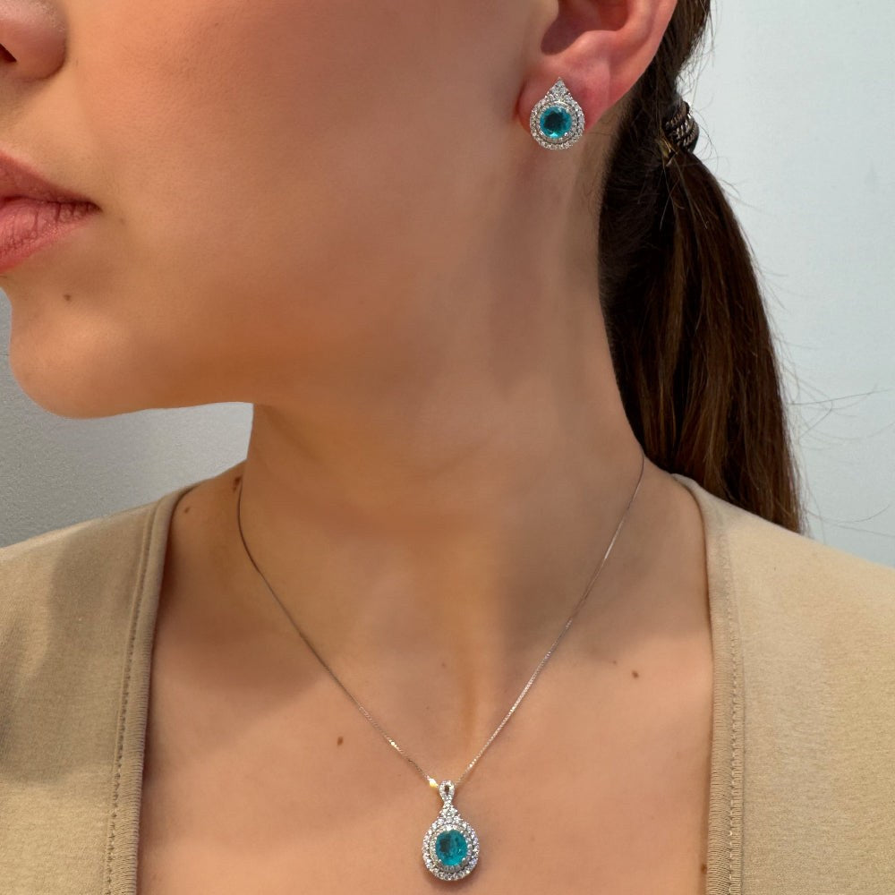 Close-up of a woman wearing turquoise gemstone earrings and necklace against a neutral background