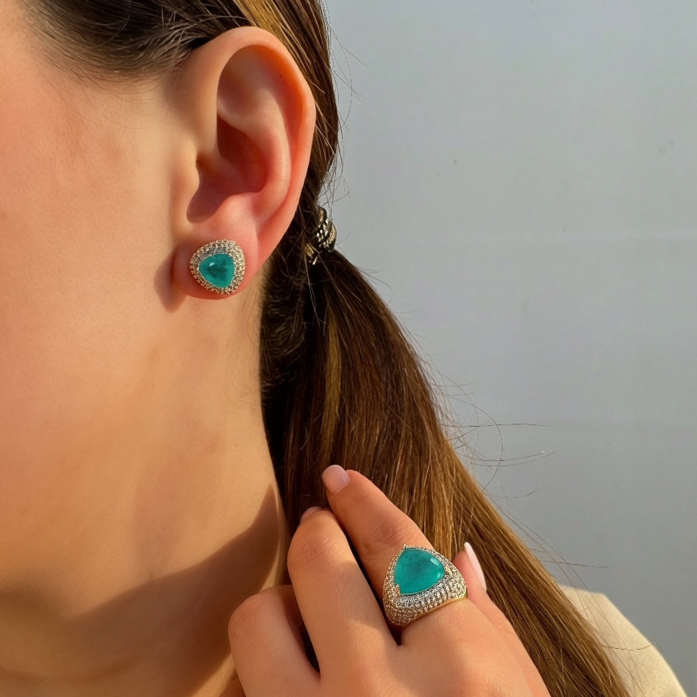 Close-up of a person wearing turquoise earrings and ring with a neutral background