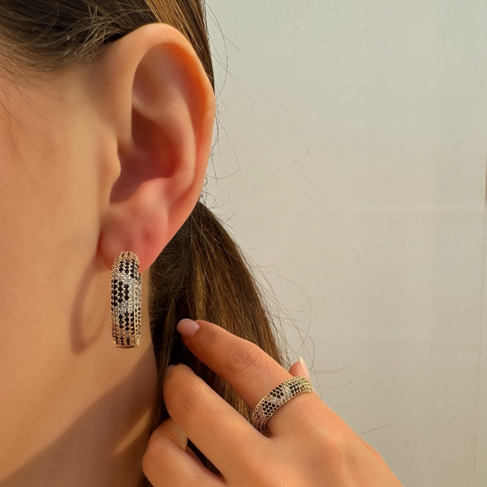 Person wearing a silver hoop earring and ring, with a neutral background