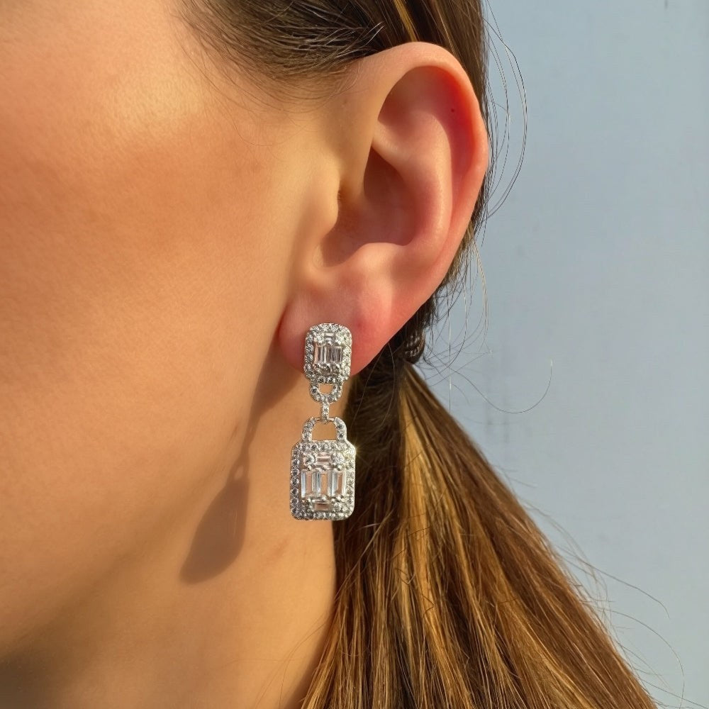 Close-up of a person wearing a silver earring with a clear gemstone against a light blue sky.