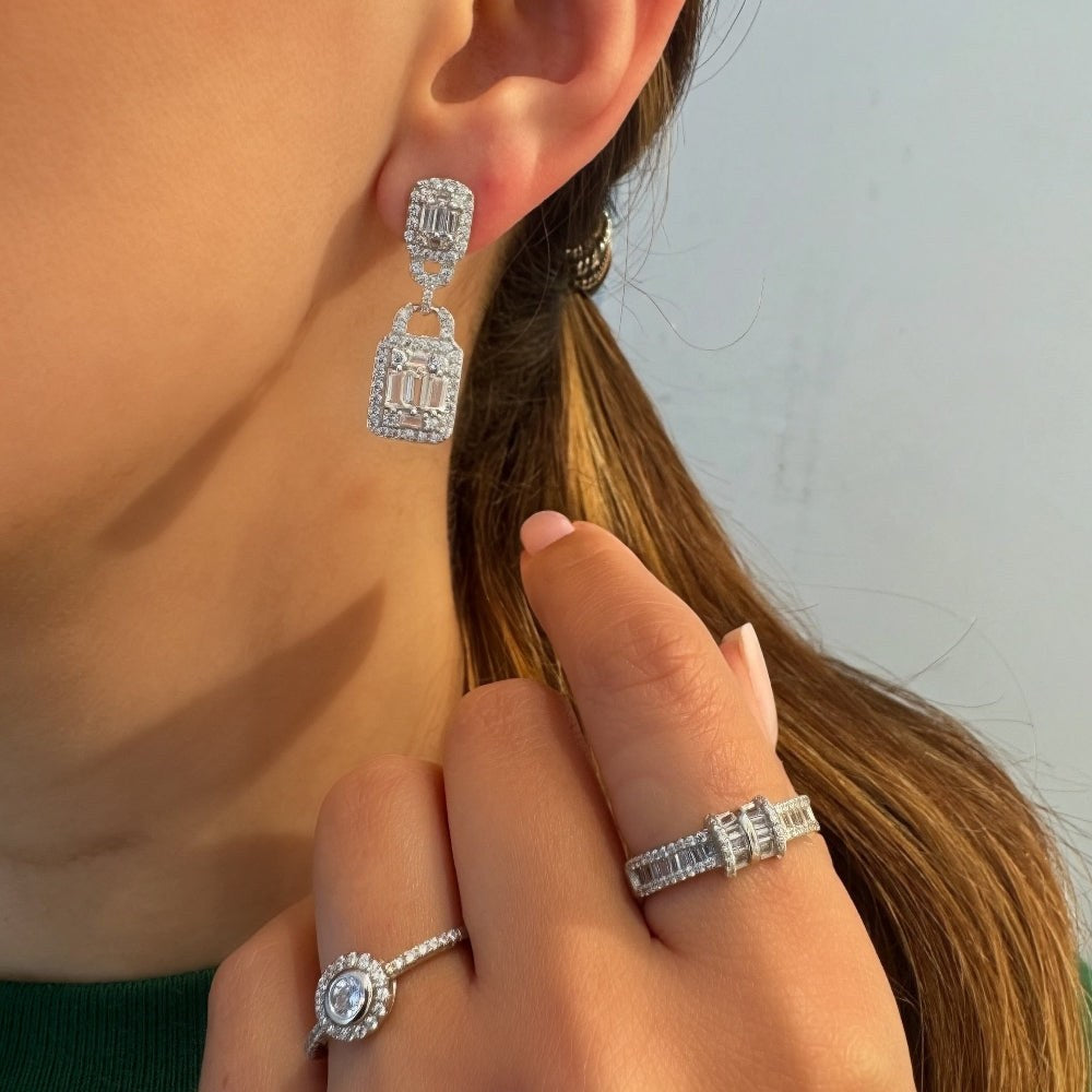 Close-up of a person wearing silver earrings and rings with a neutral background