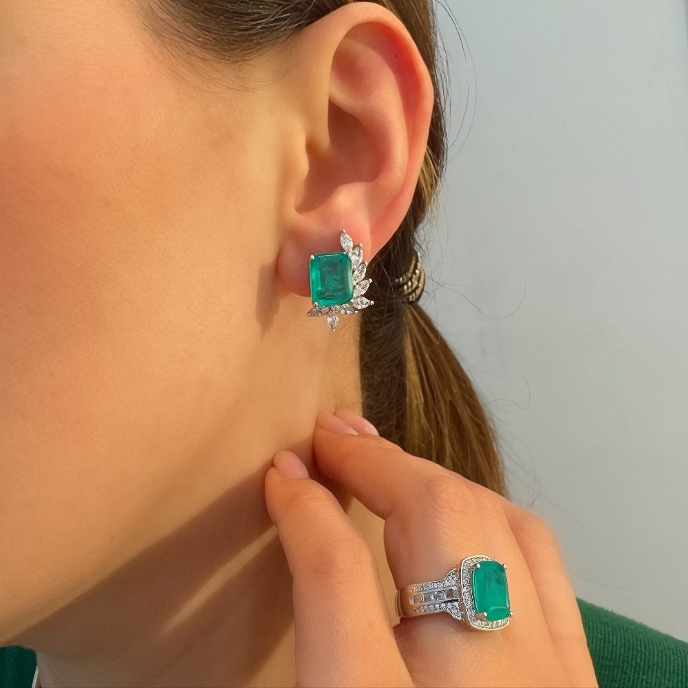 Close-up of a person wearing emerald green earrings and a matching ring.