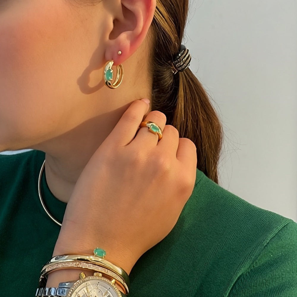 Woman wearing gold hoop earrings and a watch, with a neutral background