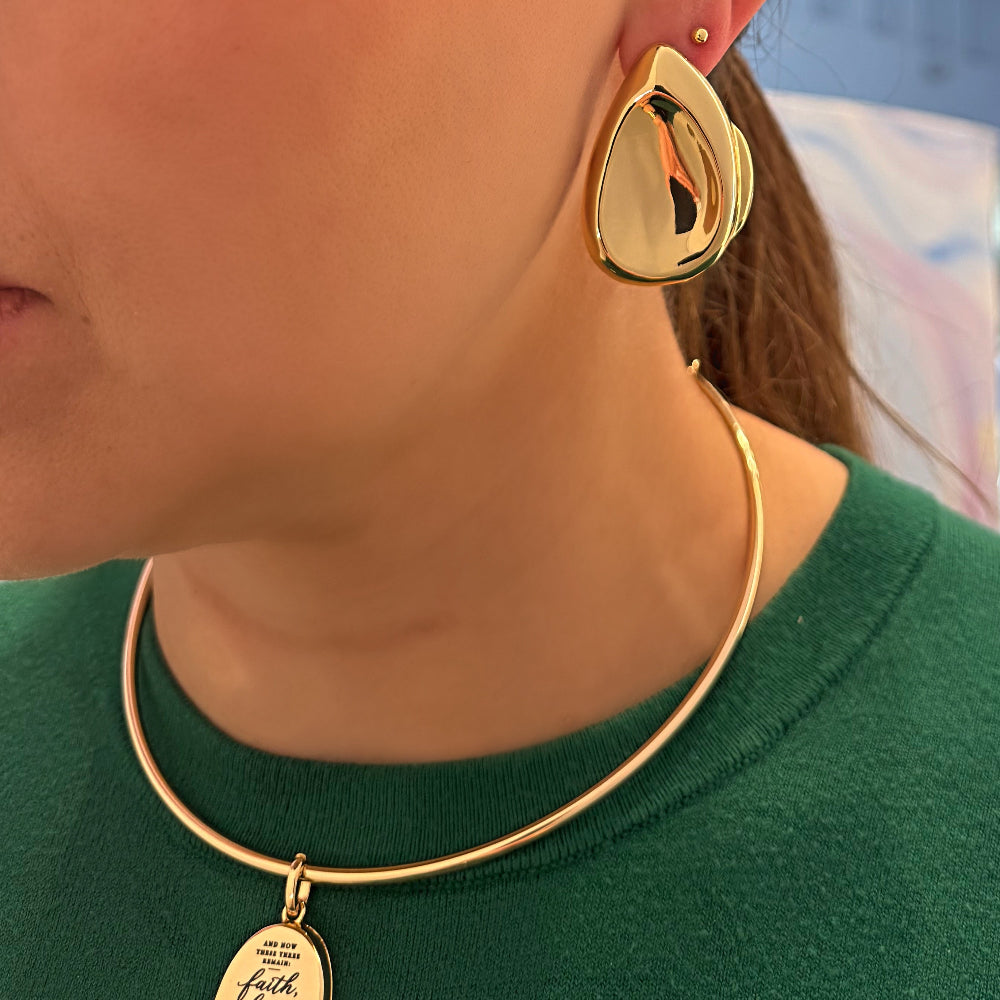 Woman wearing gold earrings and a necklace with a blurred indoor background