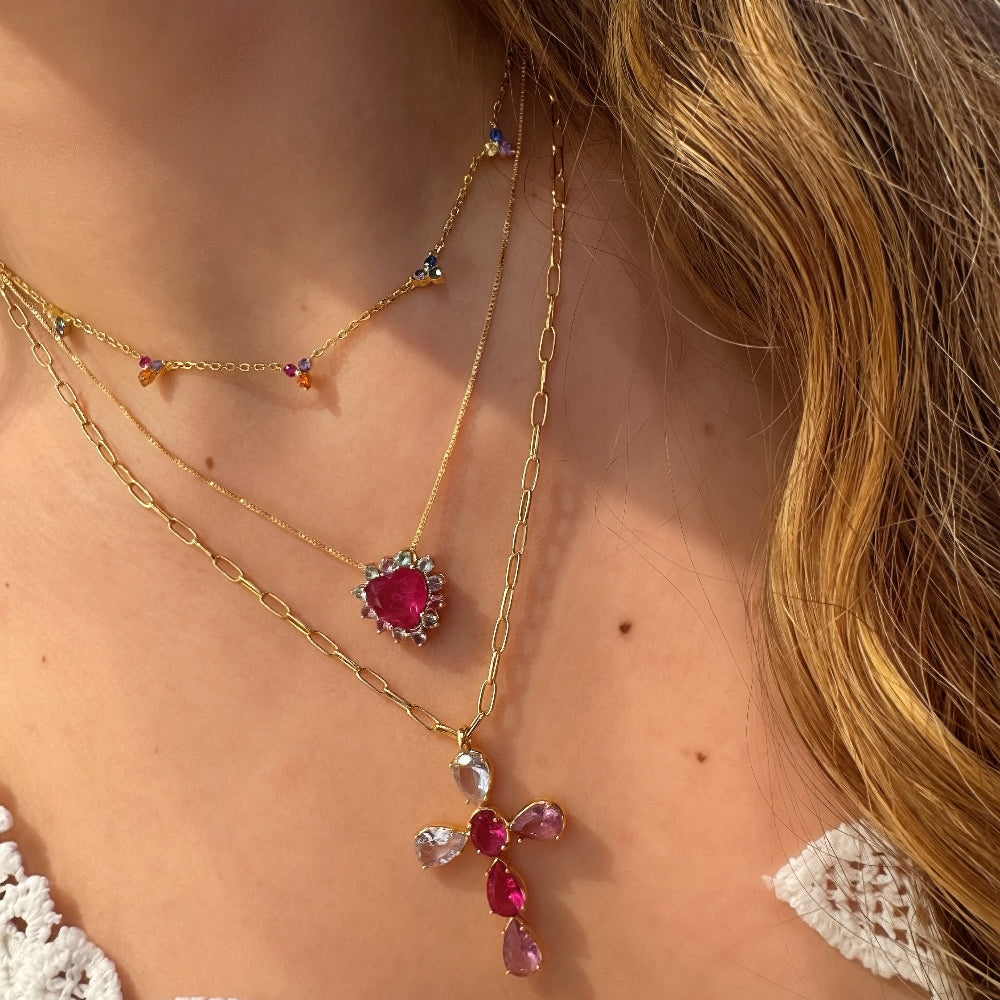 Close-up of a woman wearing a gold necklace with red and pink gemstones.