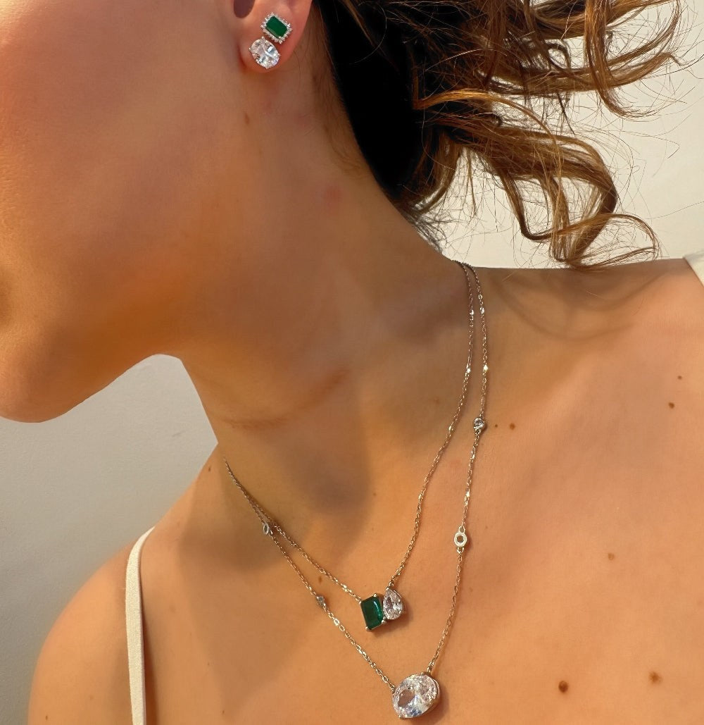 Close-up of a woman wearing a necklace and earrings with green gemstones.