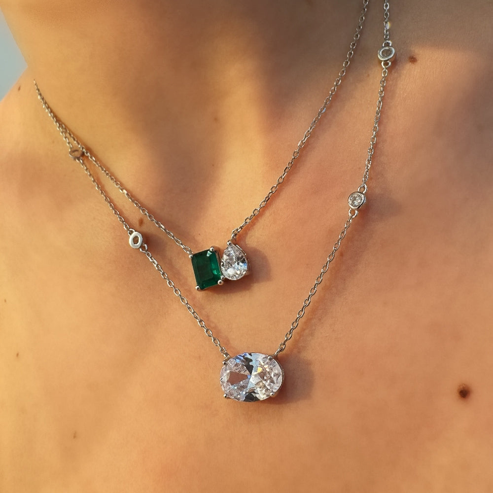 Two necklaces with gemstone pendants on a person's neck against a neutral background