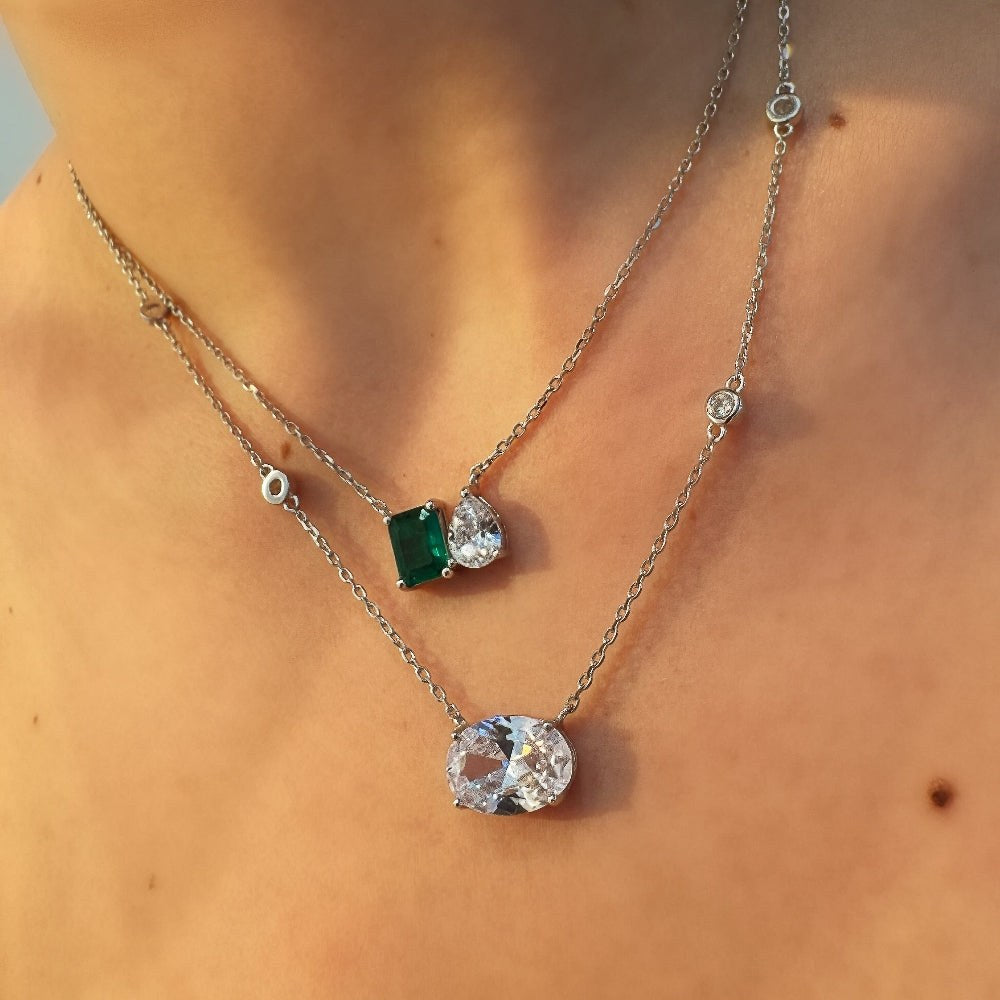 Two necklaces with gemstone pendants on a person's neck against a neutral background