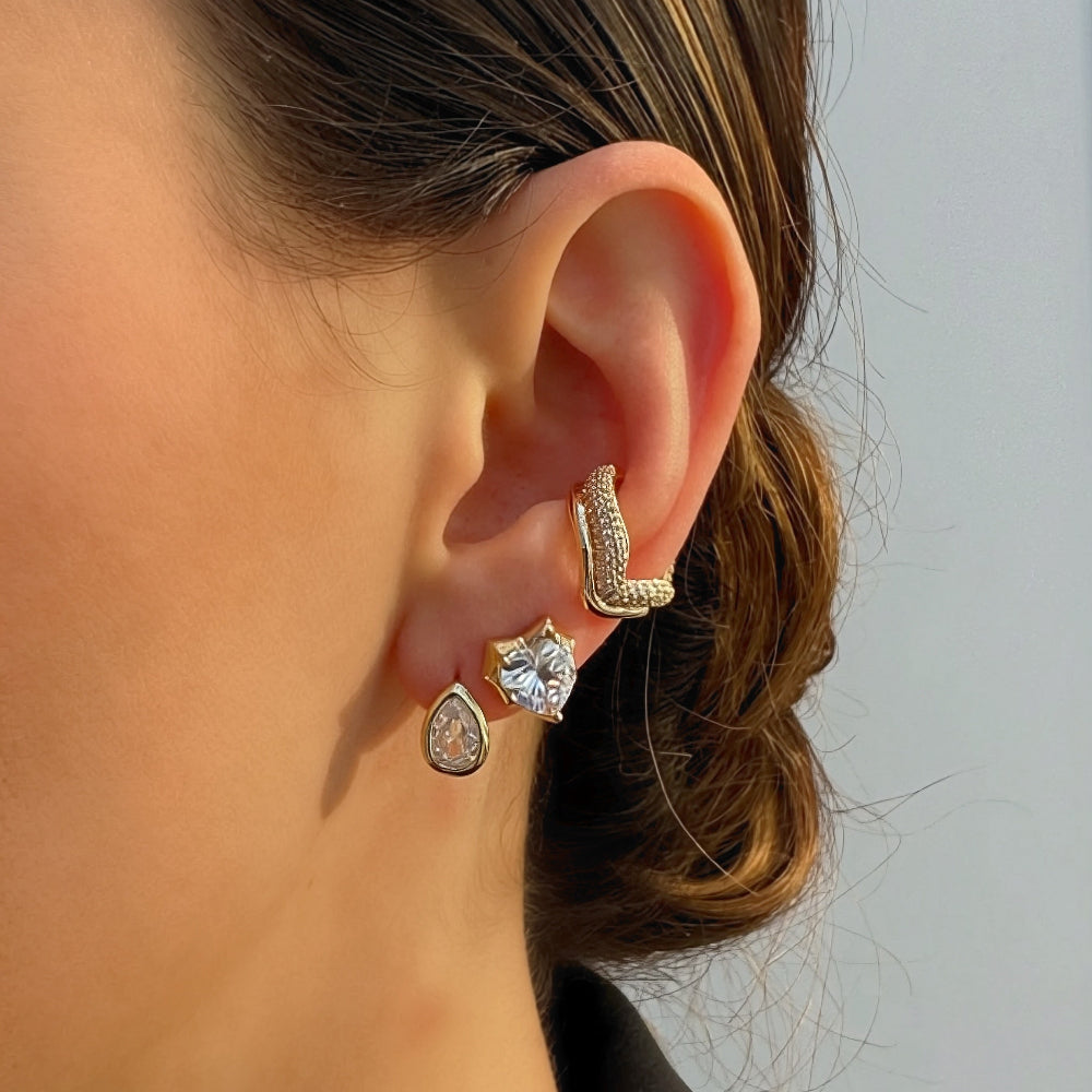 Close-up of a person's ear wearing multiple earrings with a neutral background