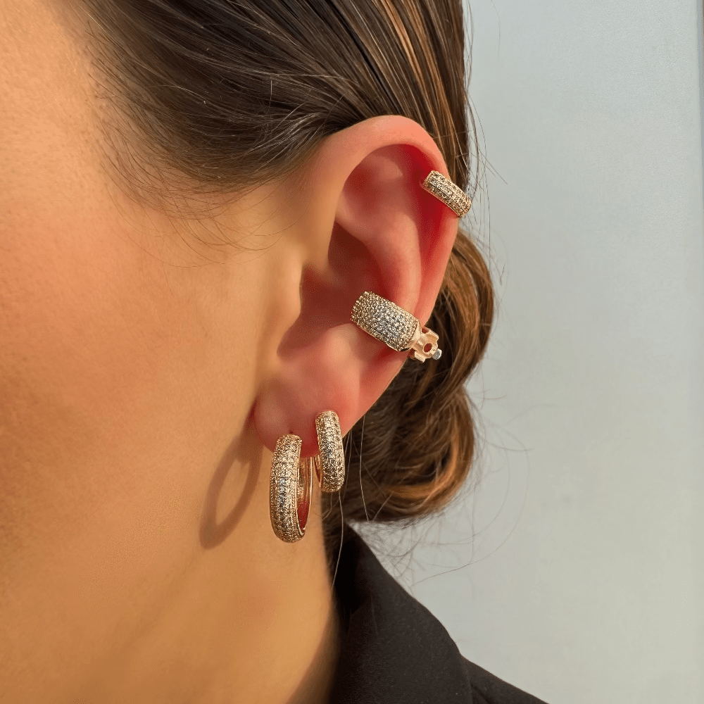 Close-up of a person's ear wearing gold hoop earrings with a plain background