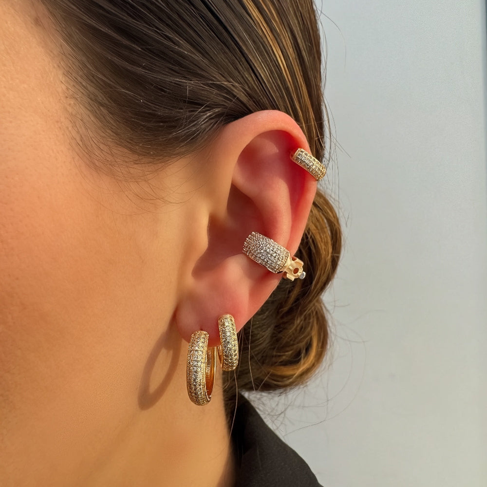 Close-up of a person wearing gold hoop earrings with diamond accents on a plain background