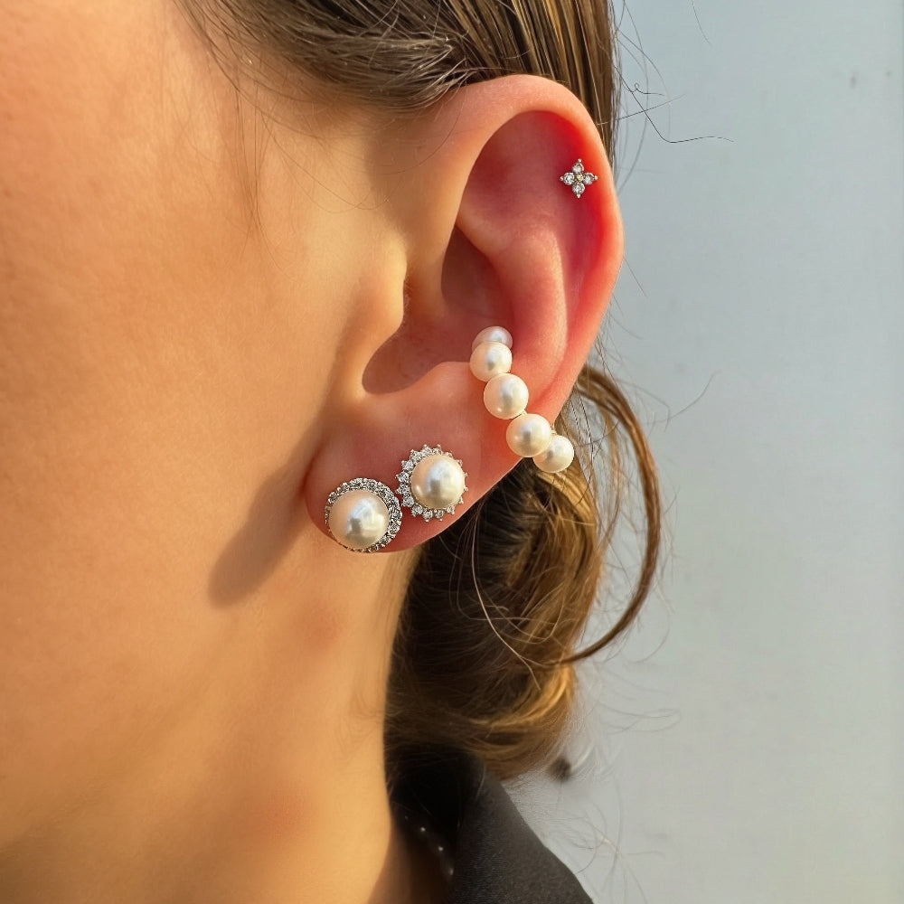 Close-up of an ear wearing pearl and diamond earrings against a neutral background