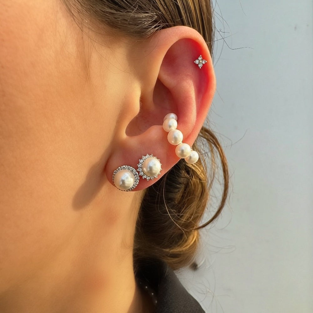 Close-up of an ear wearing pearl and diamond earrings against a neutral background
