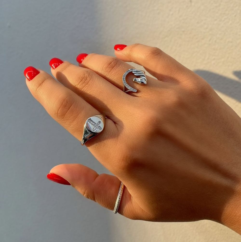 Hand with red nail polish wearing two silver rings on a neutral background