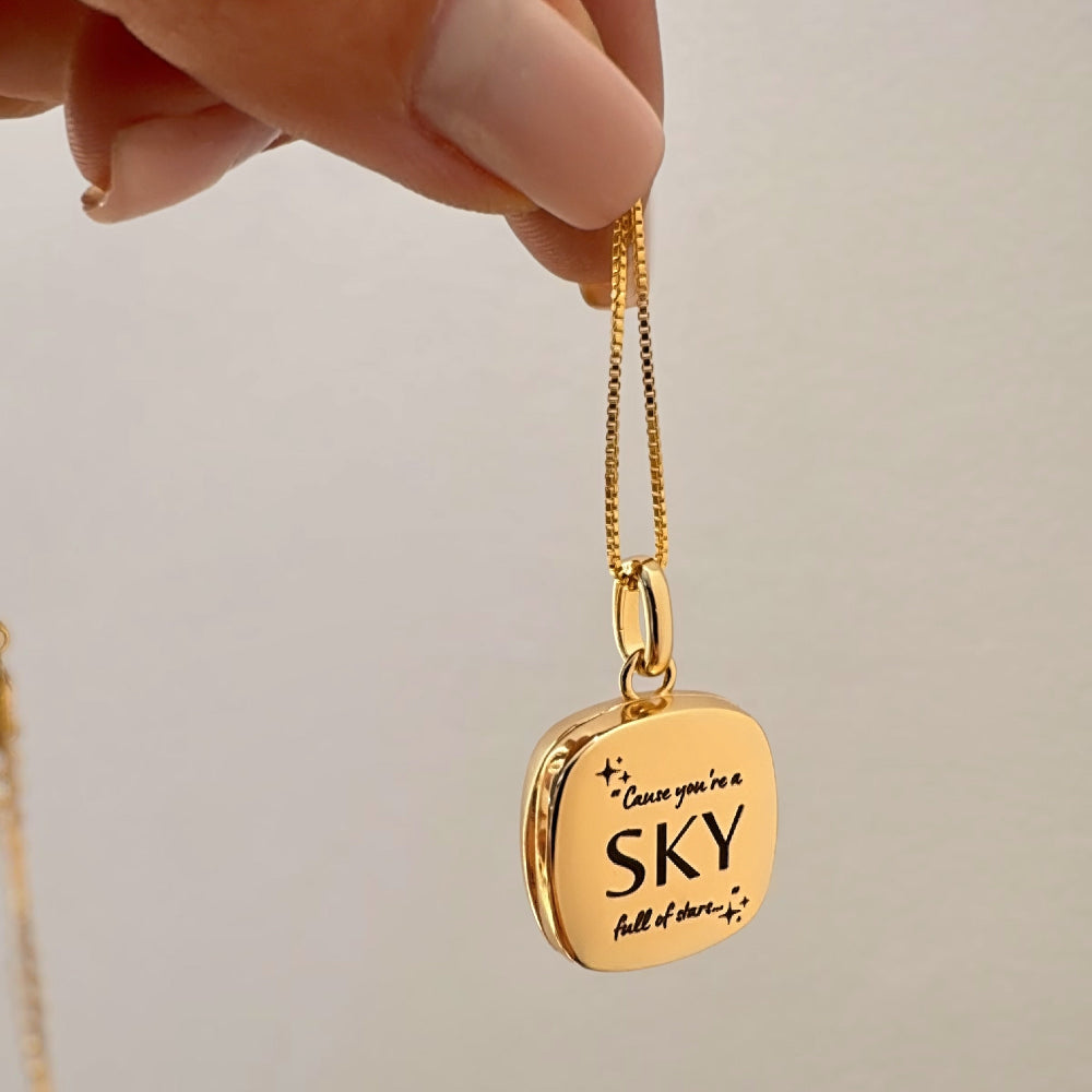 Gold necklace with a pendant held by a hand against a neutral background
