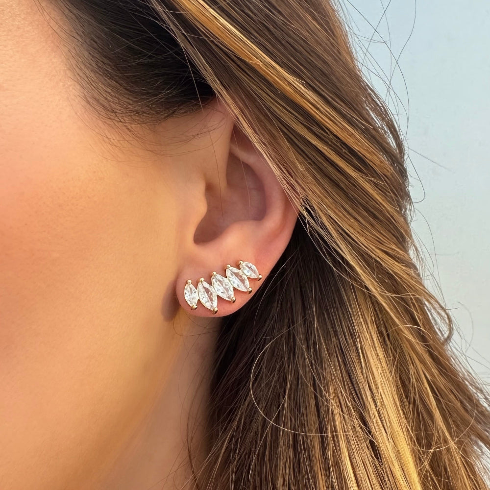 A close-up of a person's ear wearing a silver-toned ear cuff with multiple marquise-cut clear stones.