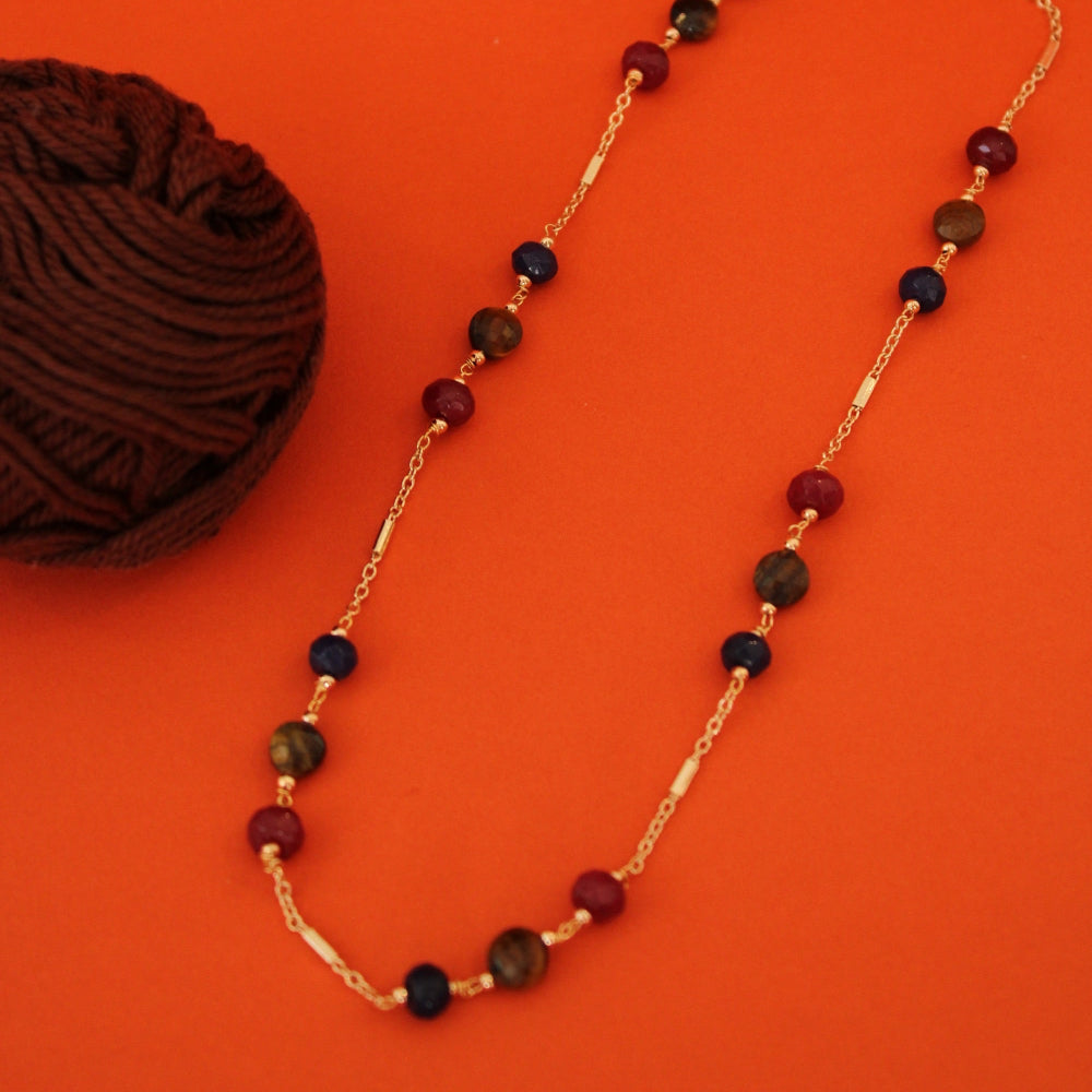 A gold chain necklace with alternating dark red, black, and brown beads, displayed on a vibrant orange background next to a ball of dark brown yarn.