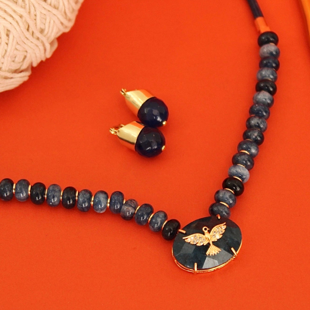 A beaded crochet hook with a round black stone pendant featuring a gold bee design, displayed alongside matching acorn-shaped earrings and two wooden crochet hooks on a bright orange background.