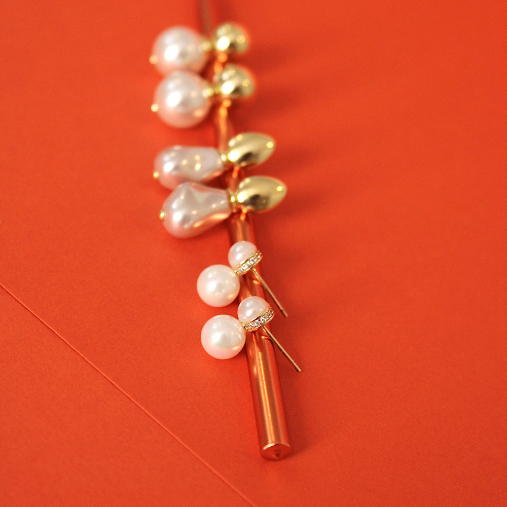 A white baroque pearls and small gold beads earrings displayed on a vibrant orange background.