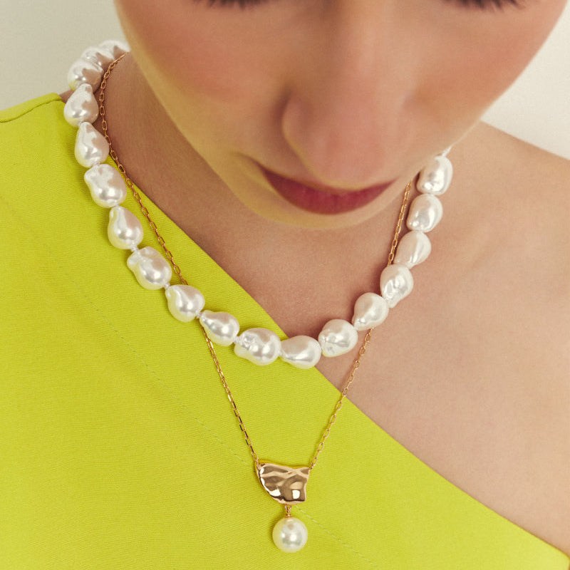 Woman wearing a pearl necklace and earrings against a plain background