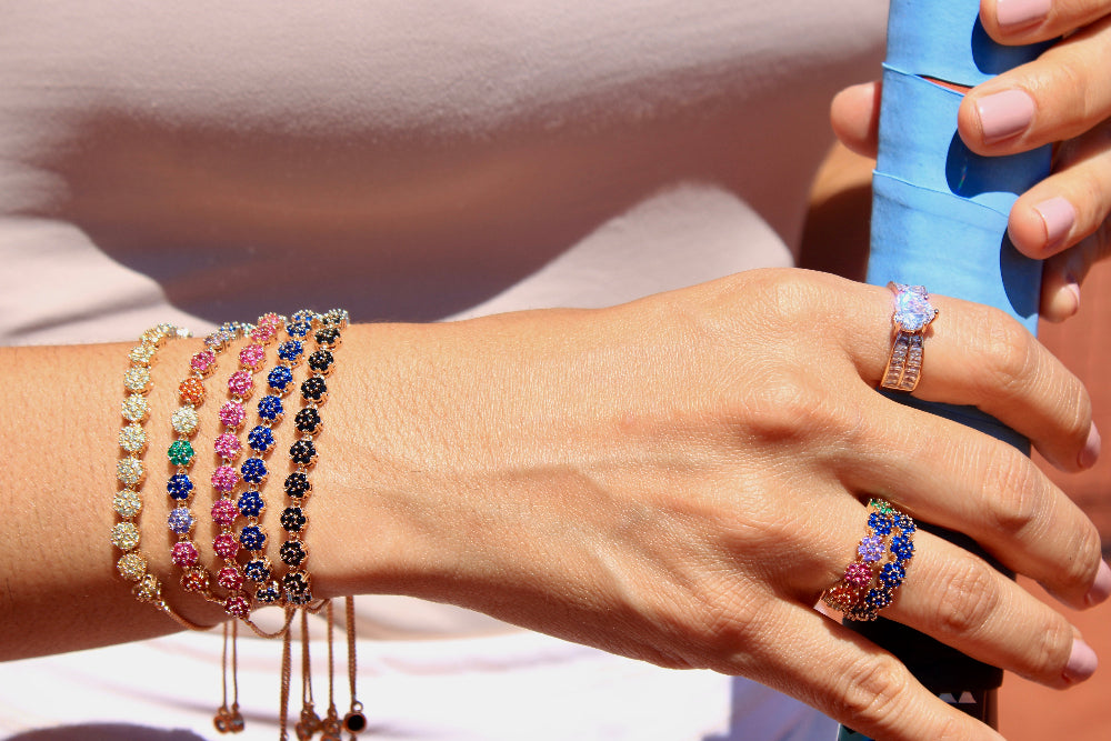 Close-up of a hand wearing colorful beaded bracelets and rings, holding a blue object.