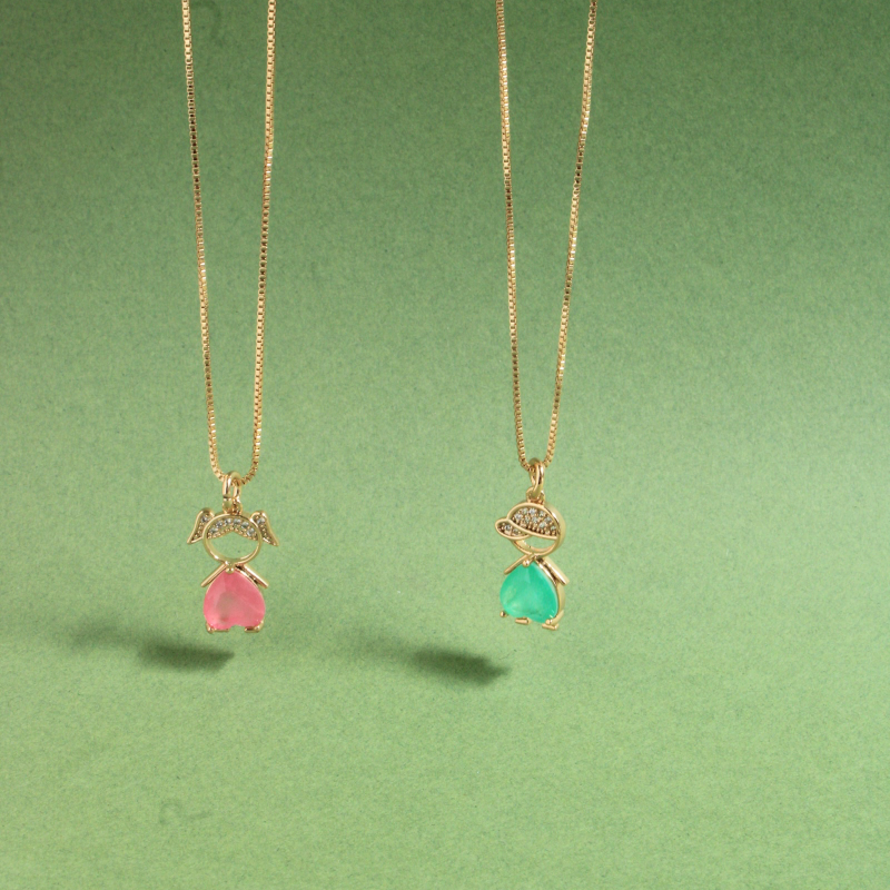 Two gold chain necklaces with small bow-shaped settings and teardrop gemstones, one pink and one green, hanging against a solid green background.