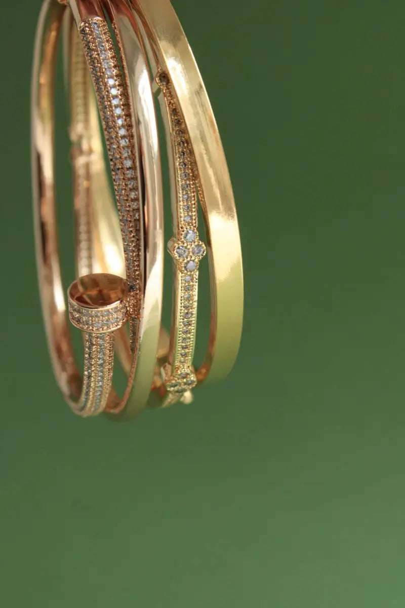 Gold bangles with diamond accents on a green background