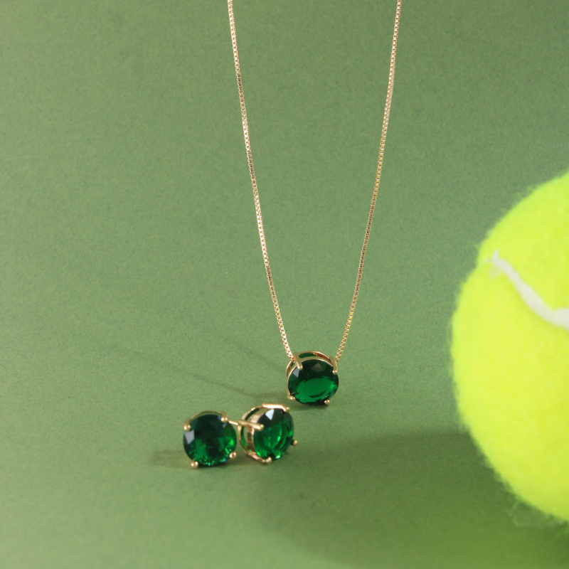 Green gemstone necklace and earrings on a green background with a tennis ball.