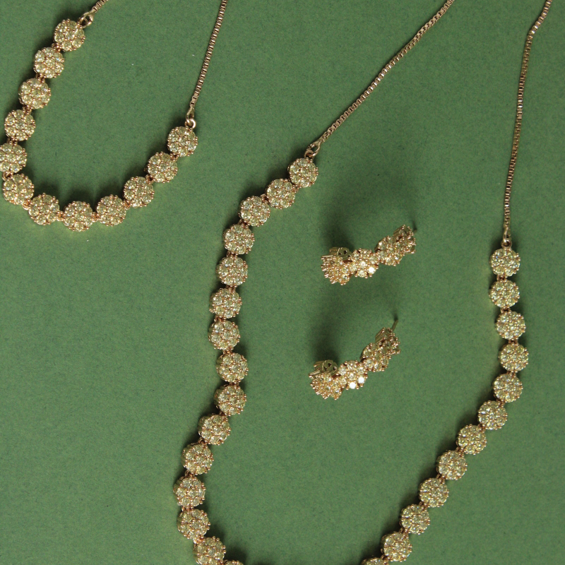 Gold adjustable necklace and adjustable bracelet with circular beads on a green background