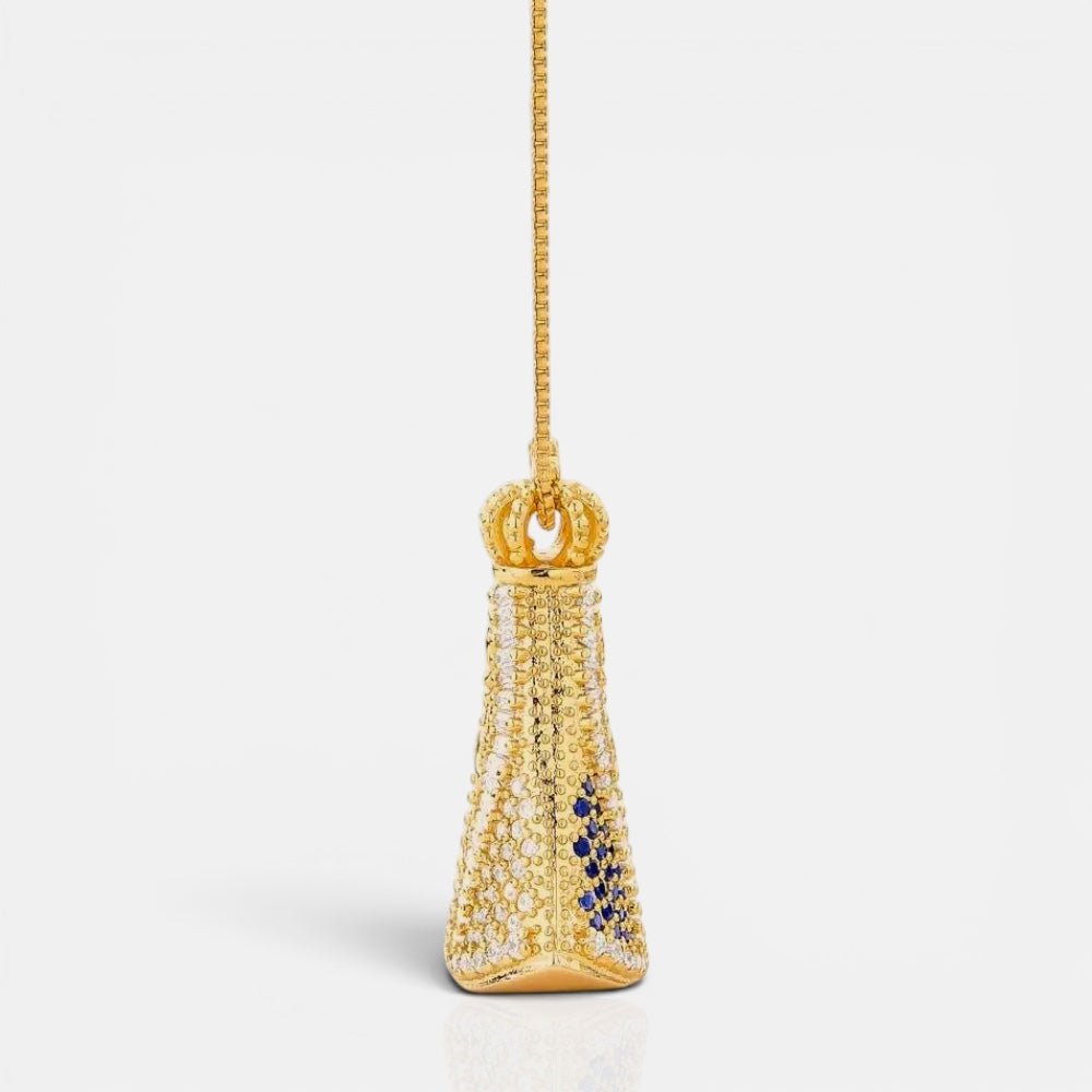A gold pendant necklace featuring a crown-shaped top and a teardrop-shaped body paved with clear crystals, accented with small dark blue stones, shown on a light gray background.