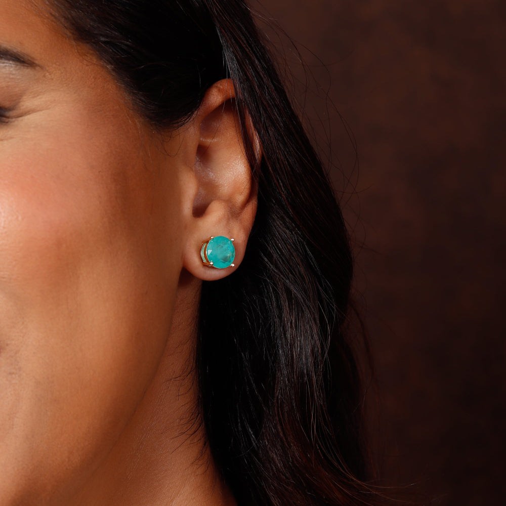 Close-up of a person wearing turquoise earrings against a brown background