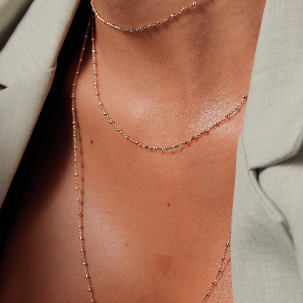Close-up of a person wearing a delicate gold necklace against a neutral background