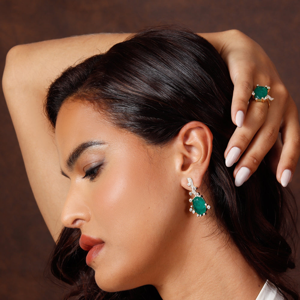 Woman wearing emerald green earrings and ring against a brown background