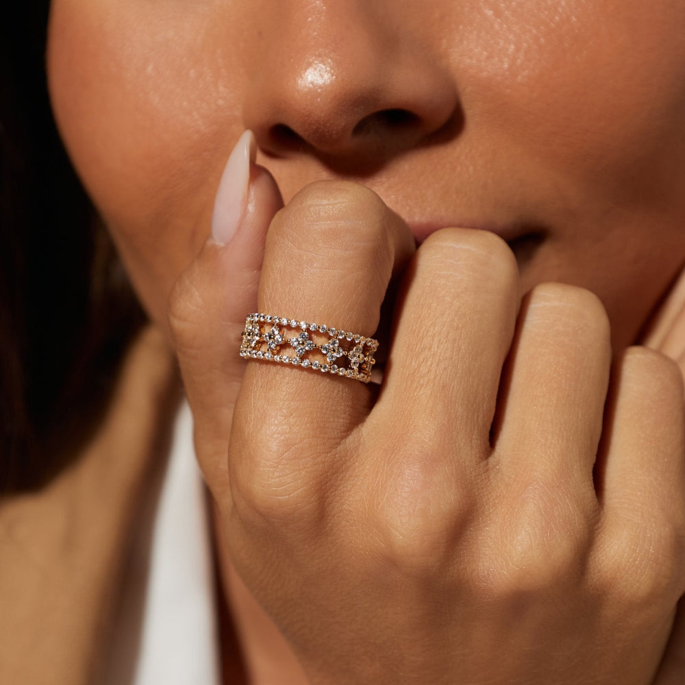 A close-up lifestyle shot of a model wearing a delicate silver band ring adorned with small clear crystals and star-shaped details. The model is wearing a white collared shirt, and the warm lighting highlights the jewelry on her finger.