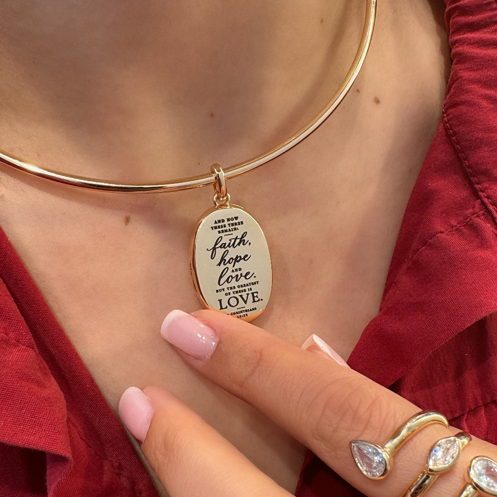 Gold bangle with a pendant worn on a wrist, with a red garment in the background.