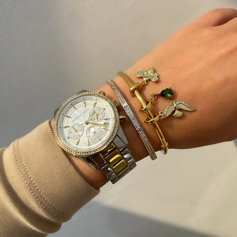 Hand wearing a gold watch and multiple bracelets on a neutral background