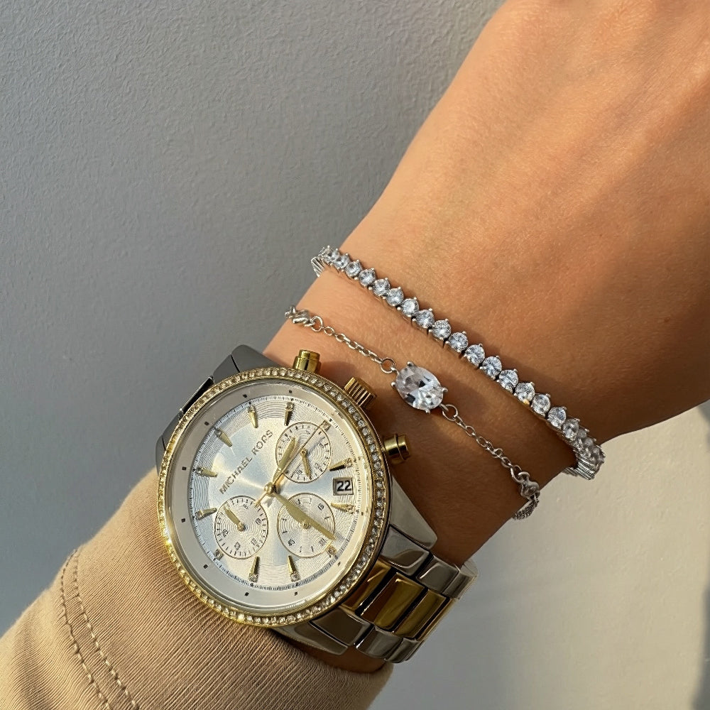 Gold watch and bracelet on a wrist against a neutral background