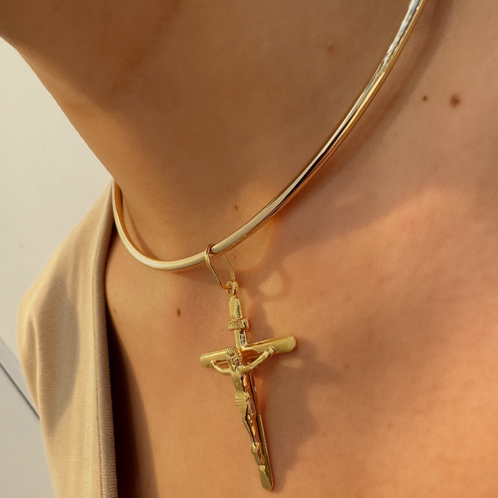Gold necklace with a cross pendant on a person wearing a beige top.