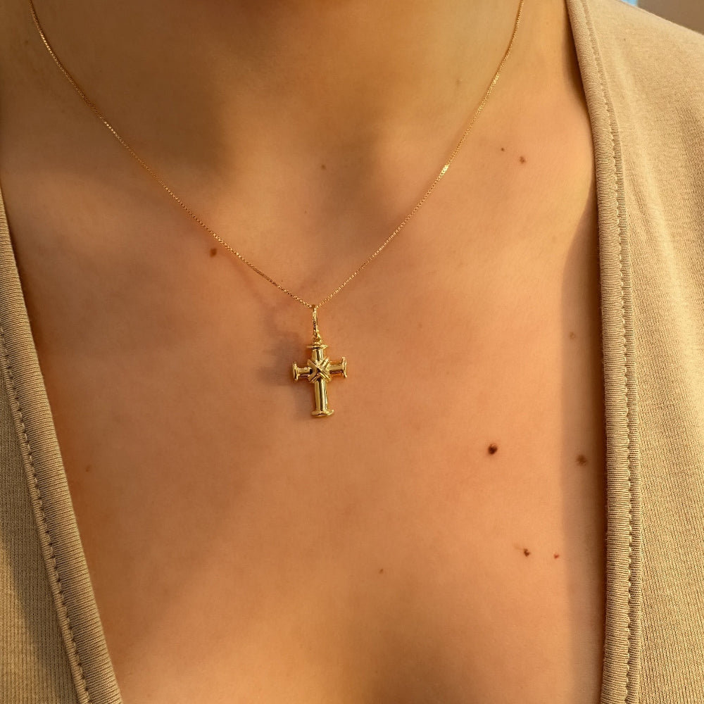 Gold necklace with a cross pendant on a person wearing a beige top.